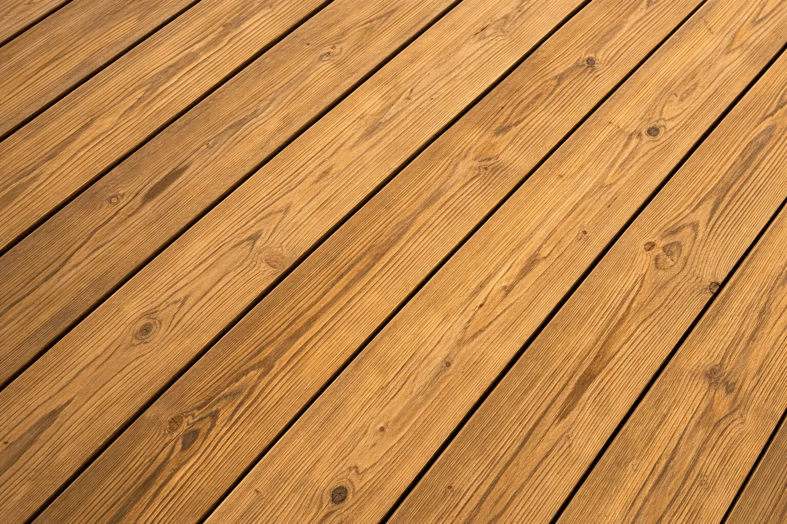 Närbild i diagonal vinkel på gyllene träplankor i ett trädäck som visar naturlig trästruktur och årsringar.